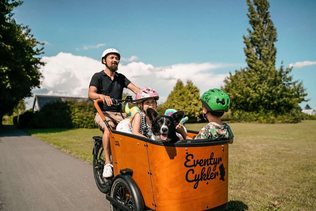 Børn og hund sidder i ladkassen på ladcykel fra EventyrCykler, mens en mand cykler